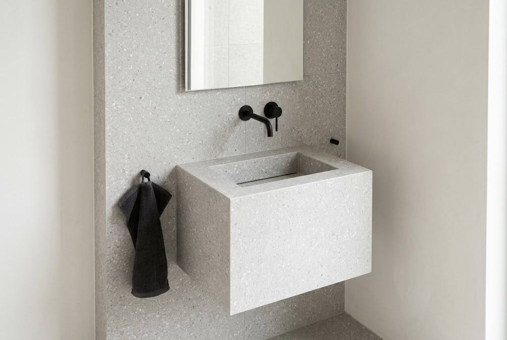 Kleiner Gäste-WC-Waschtisch mit hellgrauen Fliesen in Terrazzo-Optik und schwarzer Armatur